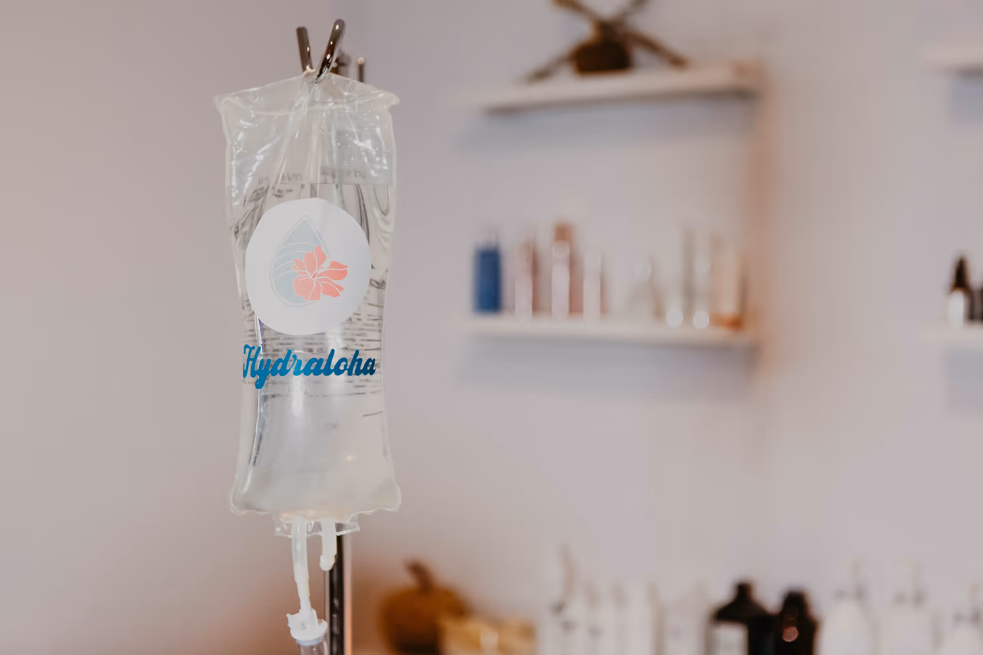 An IV bag labeled Hydraloha is in focus in a softly blurred treatment room.