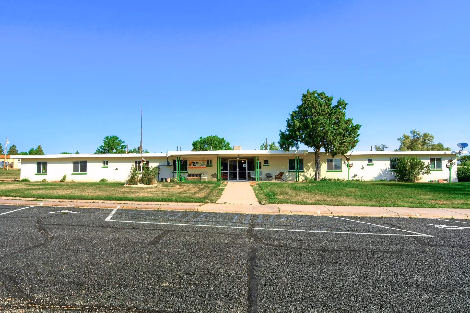 Single-story senior living building with central entrance and green doors, front lawn and parking.
