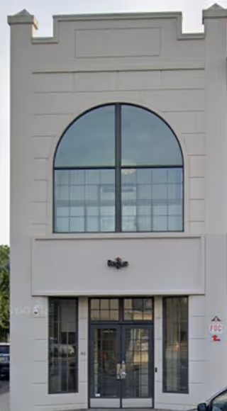 Front view of a white commercial building with a large arched window and glass doors.