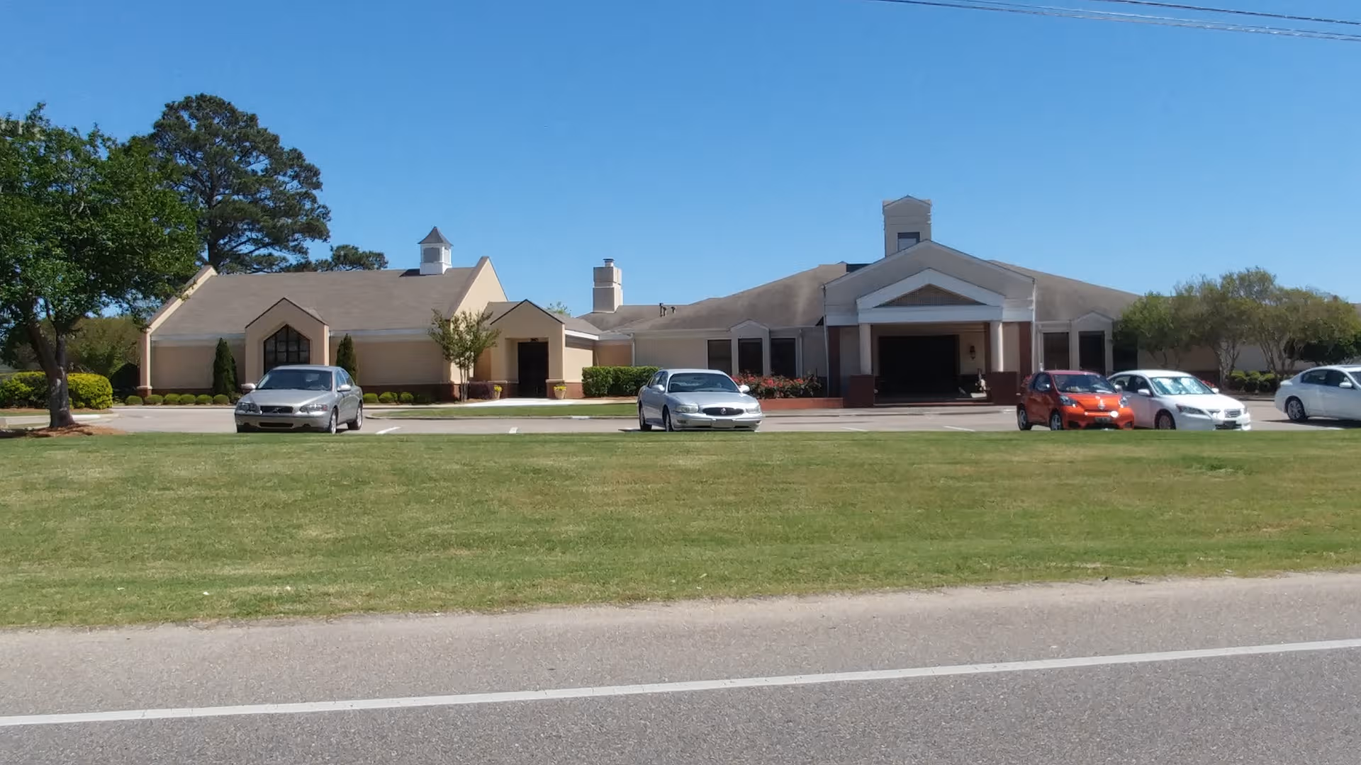 Exterior view of a Wesley Gardens facility with parked cars and a manicured lawn.