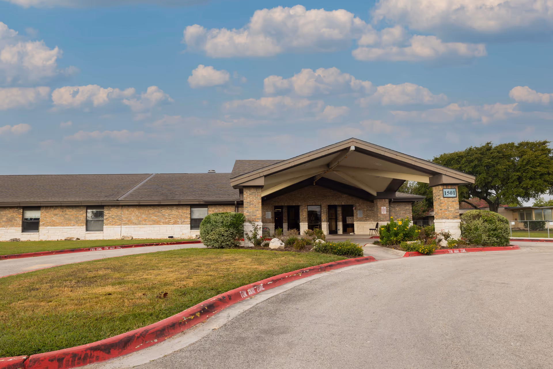 Exterior view of Parkview Nursing and Rehabilitation Center showing a single-story brick building with a covered entrance, surrounded by a driveway and landscaped greenery under a partly cloudy sky.
