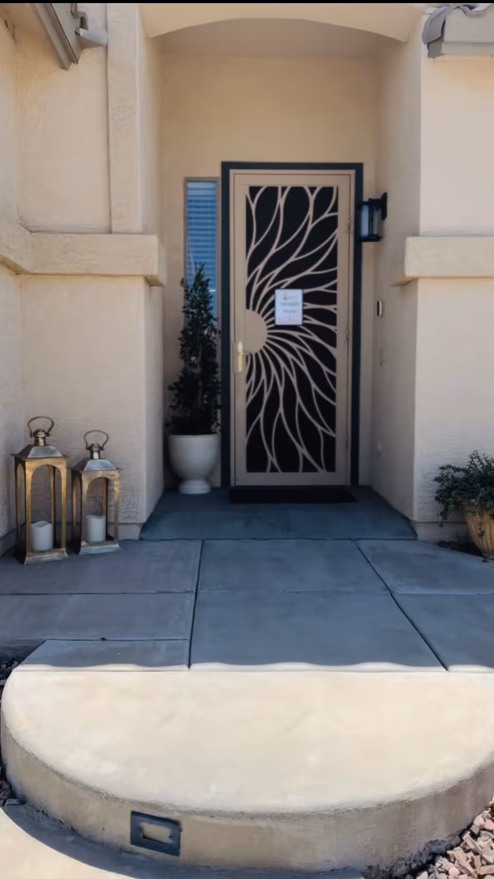 Front entrance of a beige building with decorative metal door and potted plants.