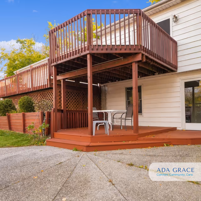 A wooden two-level deck attached to a beige house with outdoor chairs.