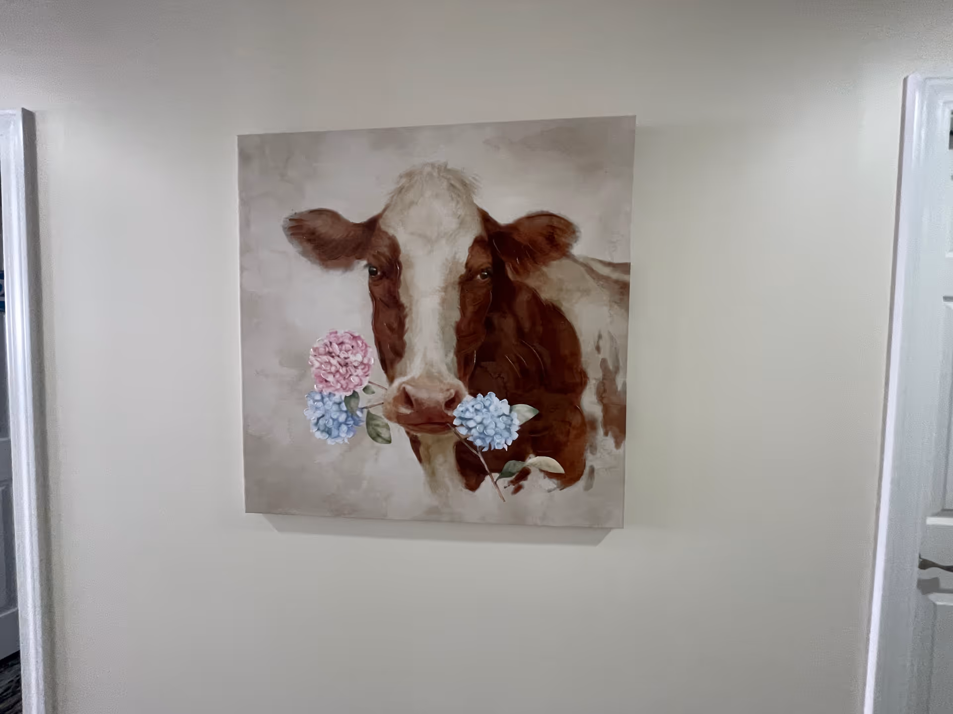 A cow painting with hydrangeas hangs on a beige interior wall.