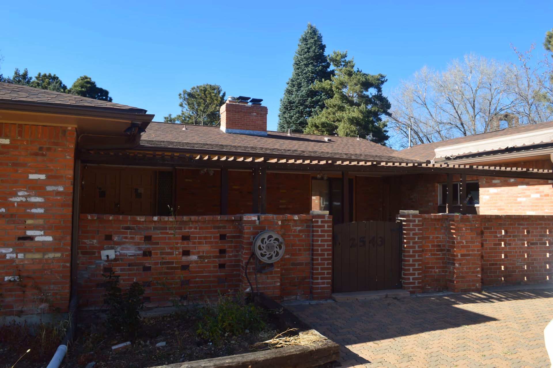 Single-story red brick building with a low brick courtyard wall and wooden gate under a clear blue sky.