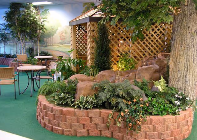 Indoor courtyard garden with a brick planter, gazebo, trees, and round tables with chairs.