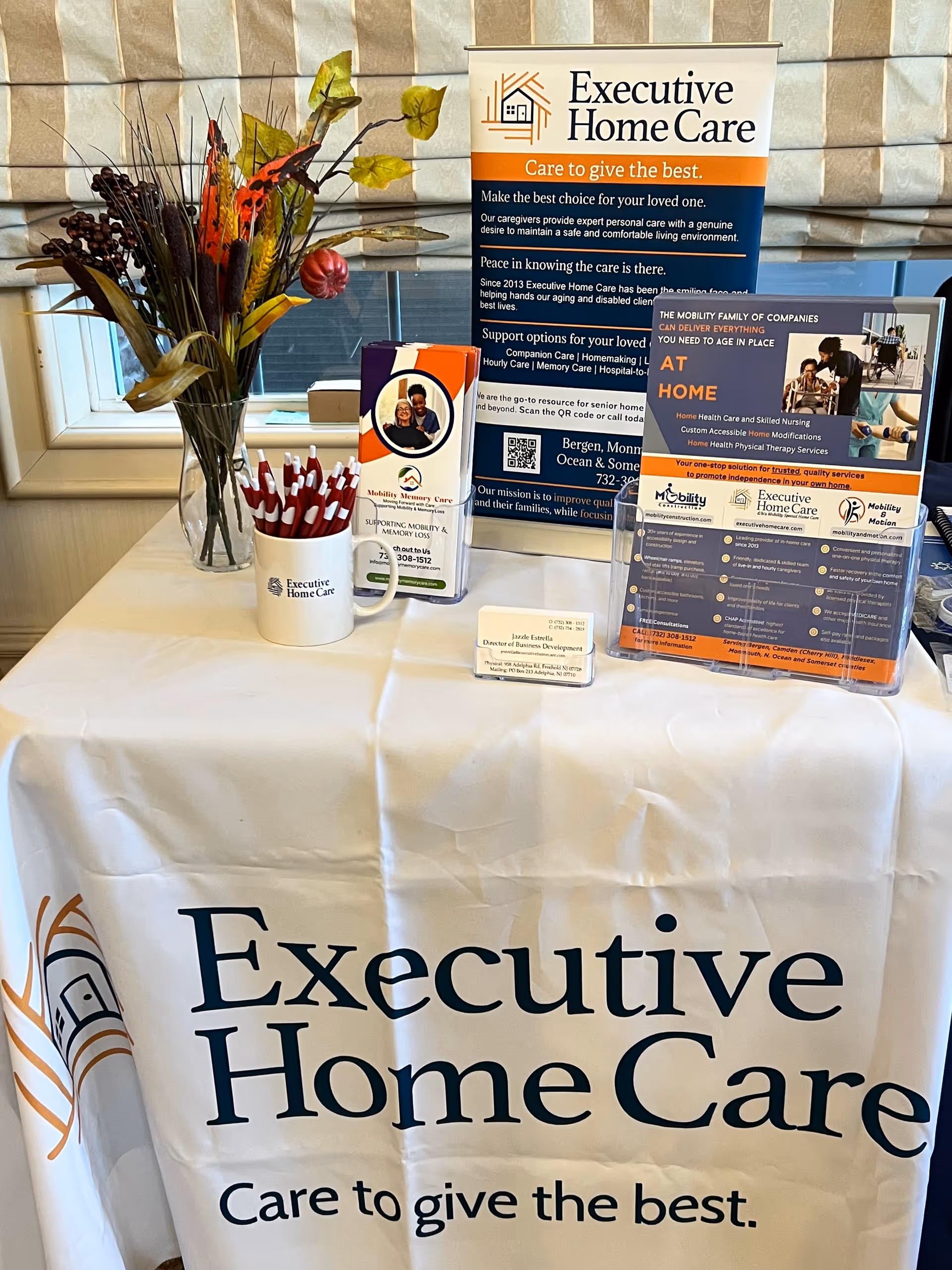 Indoor display table with Executive Home Care banners, brochures, and a vase of flowers.