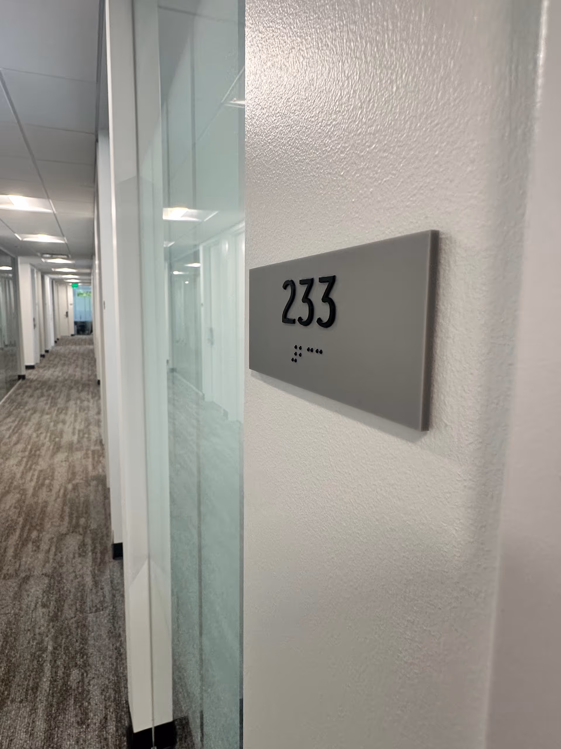 Hallway inside a senior living facility with glass-walled offices and a brushed sign reading 233.