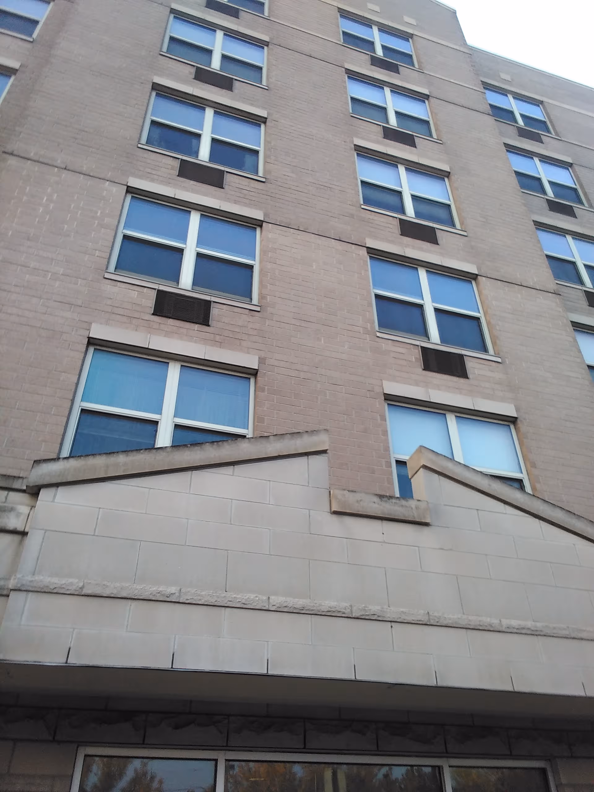 Tall beige brick senior living building with multiple windows and entrance steps.