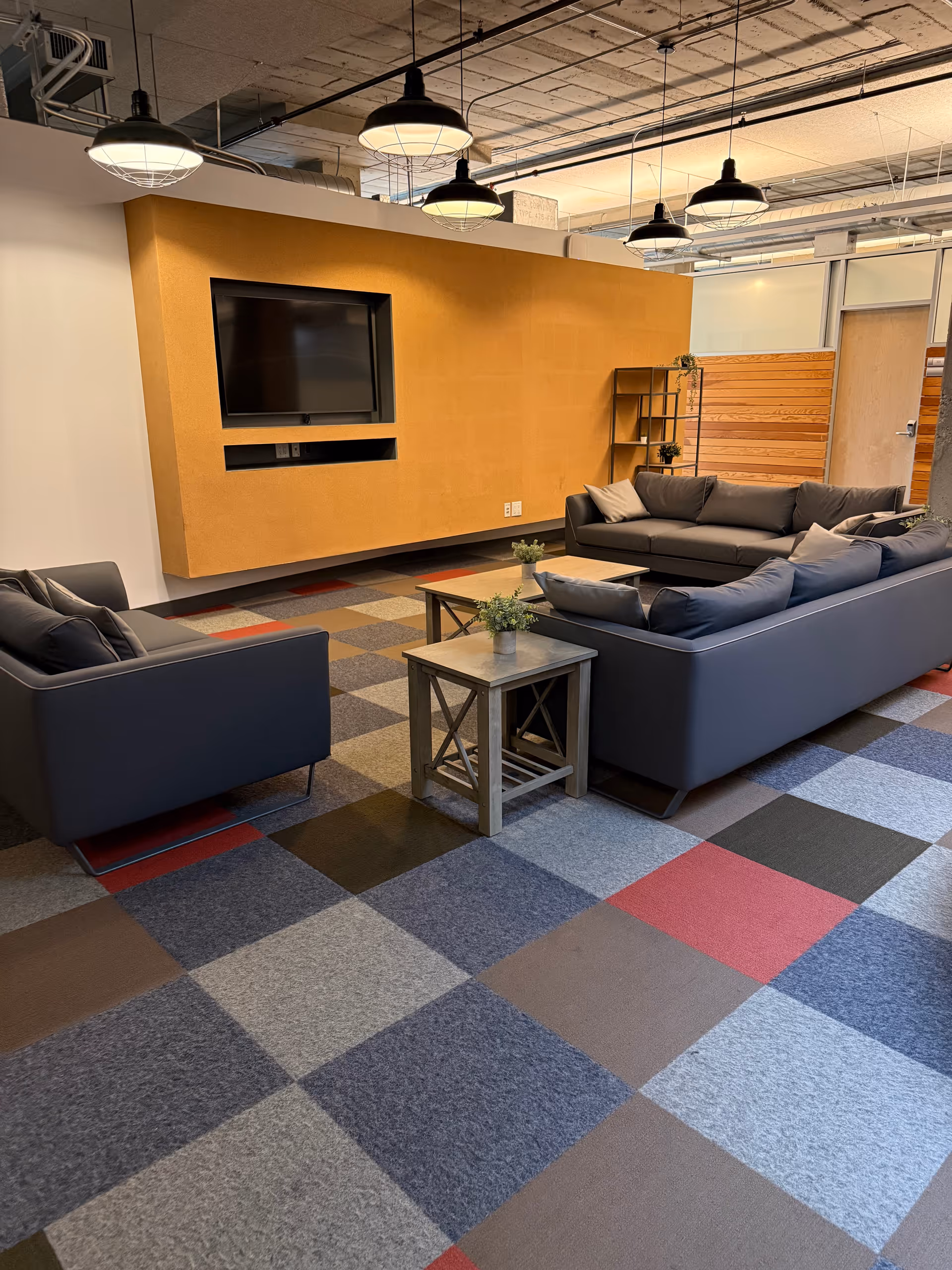 A modern lounge area with dark sofas, a wall-mounted TV, and colorful carpet.