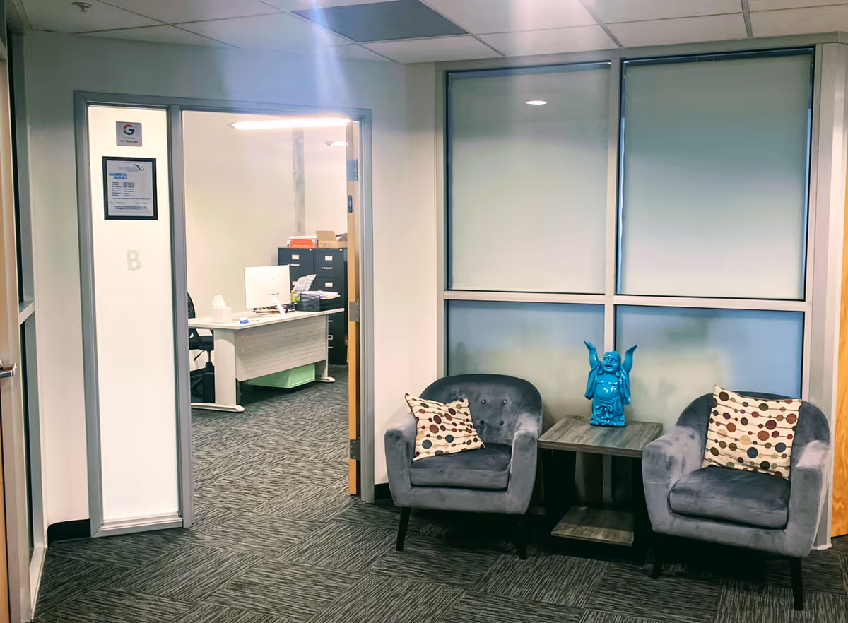 Reception seating area with two blue chairs, a small table, and an office doorway.
