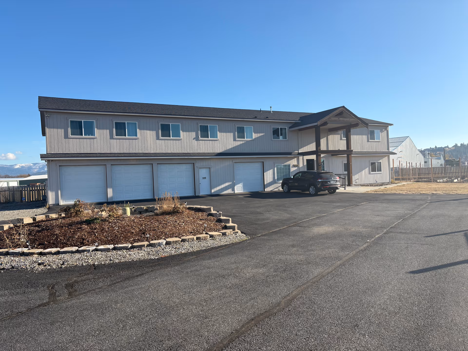 Two-story senior living facility exterior with multiple garage doors and a parked car.