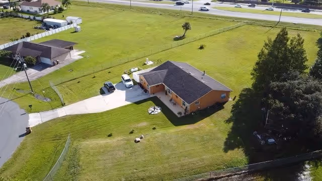 An aerial view shows a single-story orange building with a driveway and expansive green lawn.