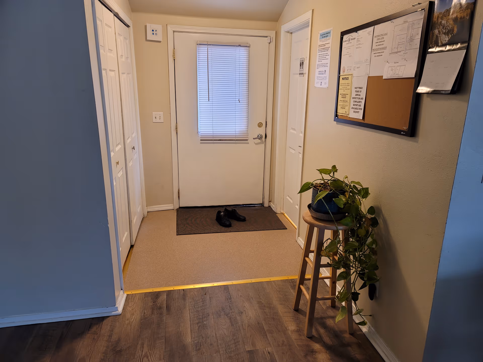 Hallway entry with white doors, a small potted plant, bulletin board, and shoes near the door.