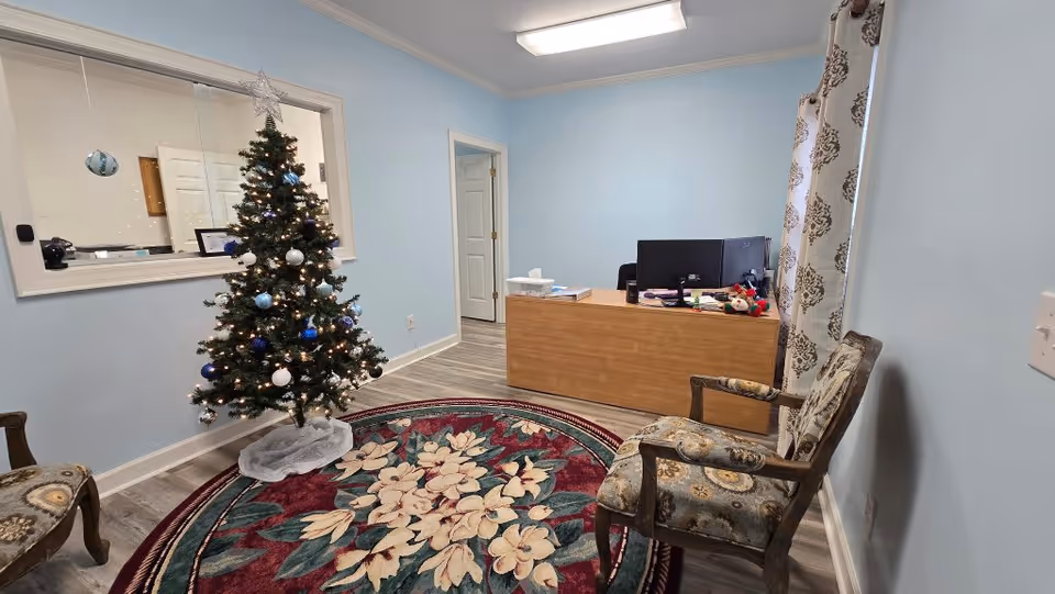 Reception area with a Christmas tree, desk, and patterned chairs in a light blue room.