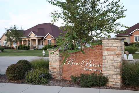 Brick entrance sign reading "River Birch Senior Living" with landscaping and a residential building behind it.