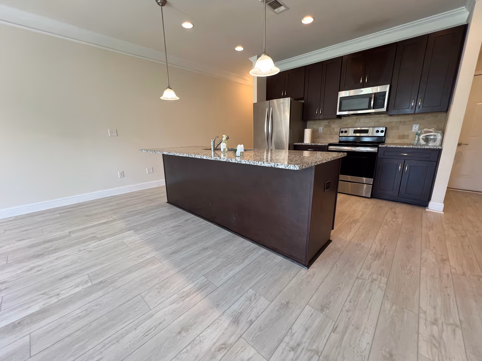 Modern kitchen with granite island, dark cabinets, and stainless steel appliances.