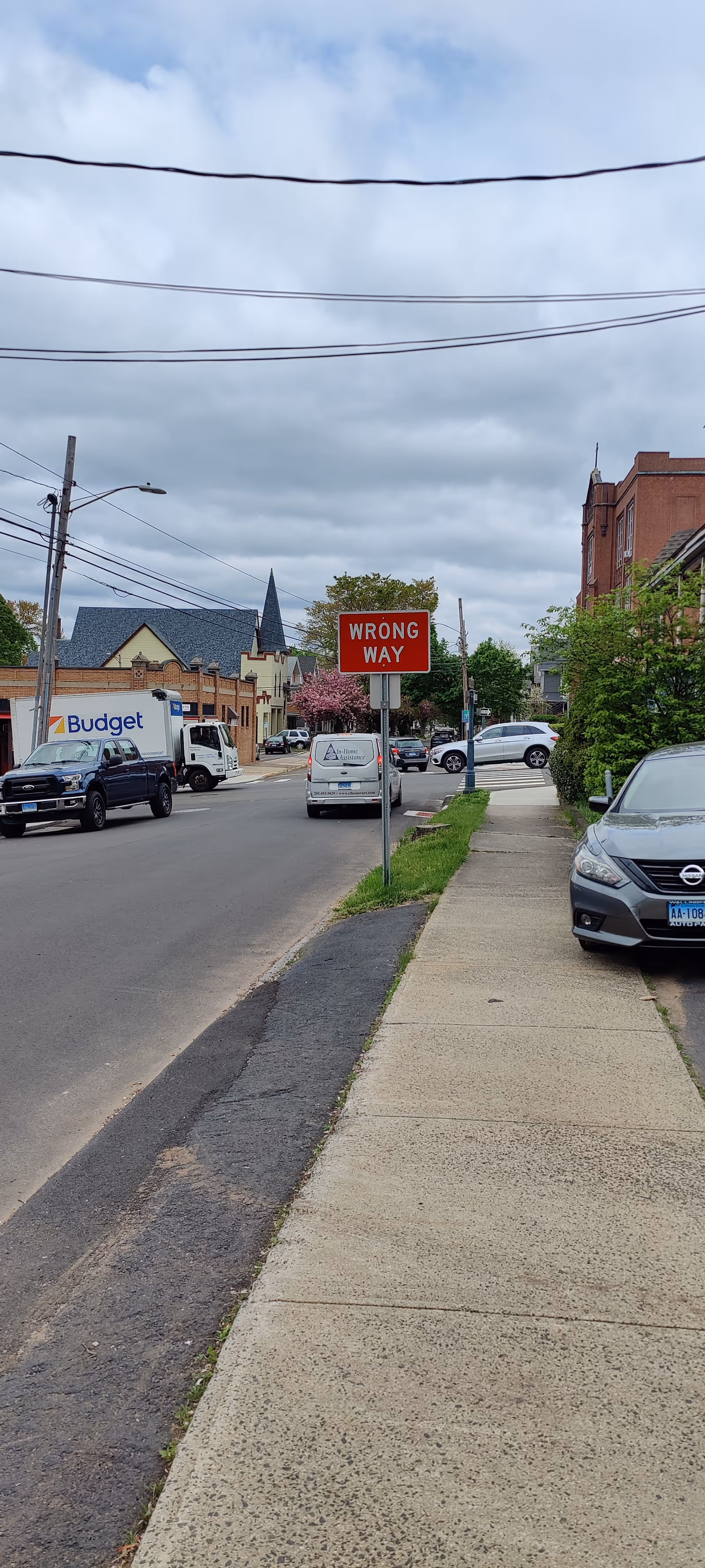 Exterior street view with sidewalks, parked cars, and a prominent Wrong Way sign near storefronts.