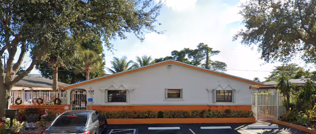Front view of a single-story white building with orange trim, parking spaces, a parked car, and trees.