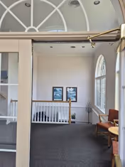 Interior of a senior living facility lounge with framed pictures and seating near a railing.