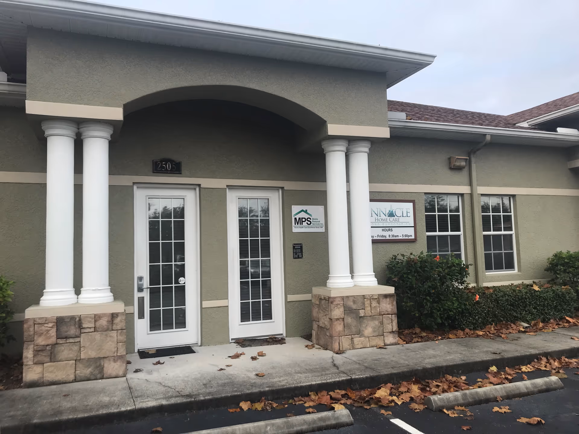 Exterior of a senior living facility entrance featuring columns and glass doors.