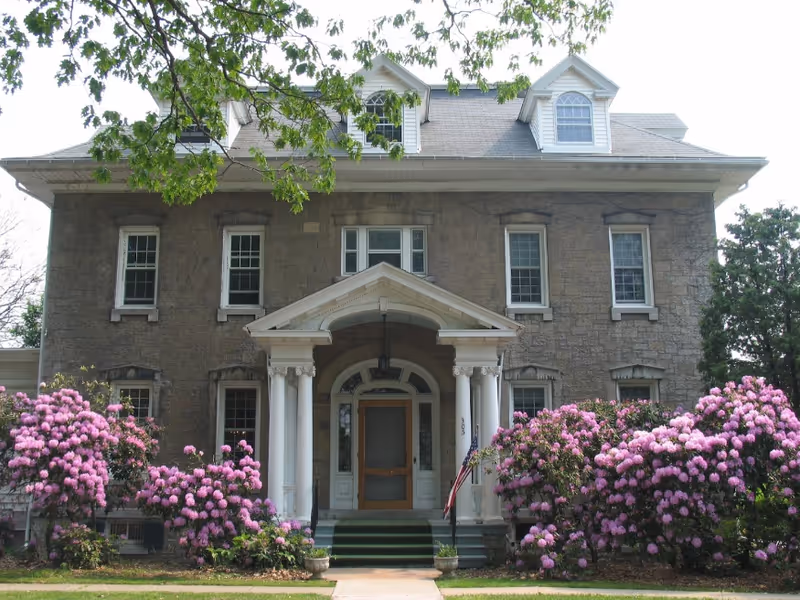 Front view of Whispering Oaks Waverly building with columns and blooming pink shrubs.