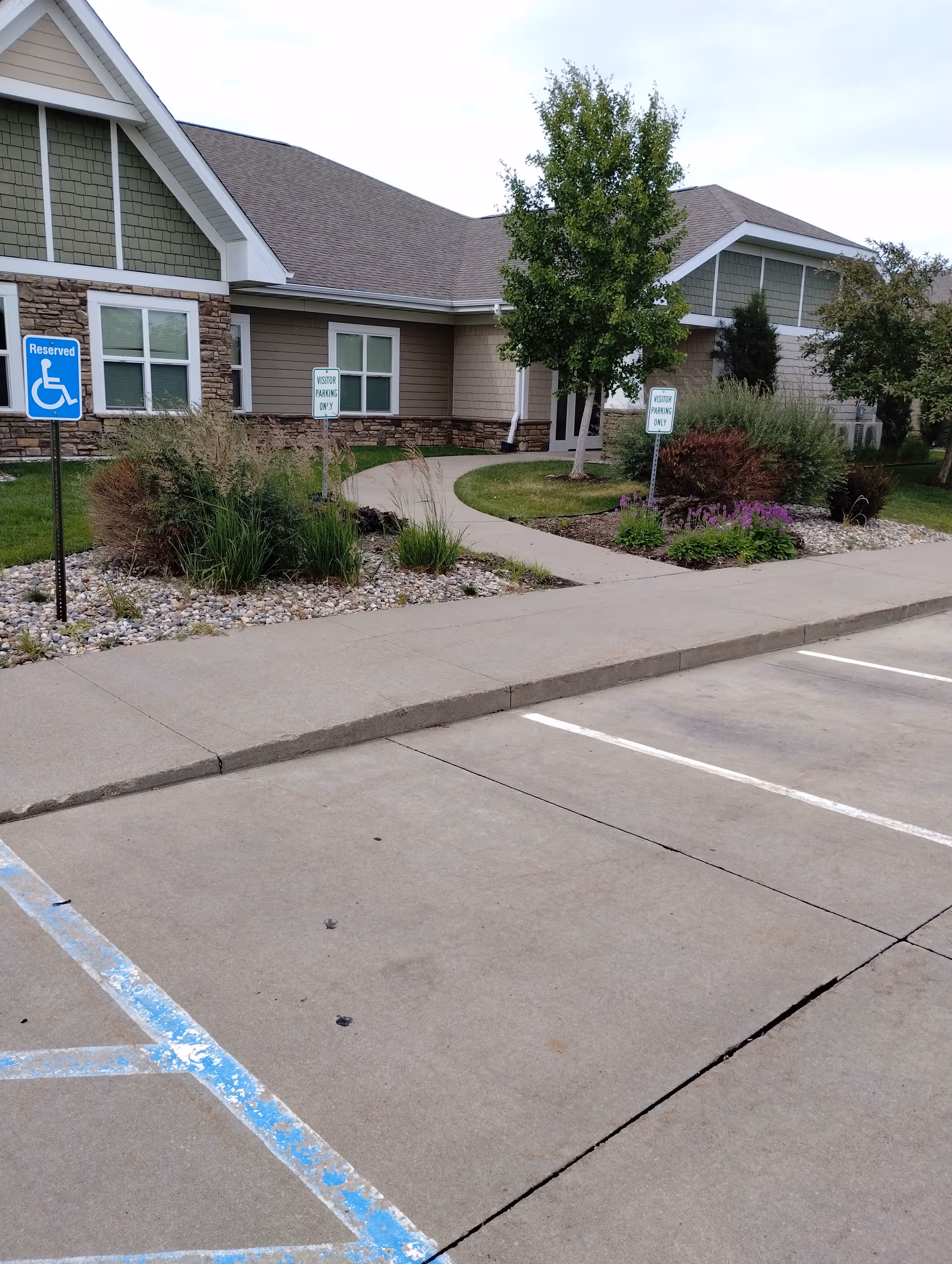 Exterior view of Hearthstone - Pella with a curved walkway, landscaping, and a parking lot.