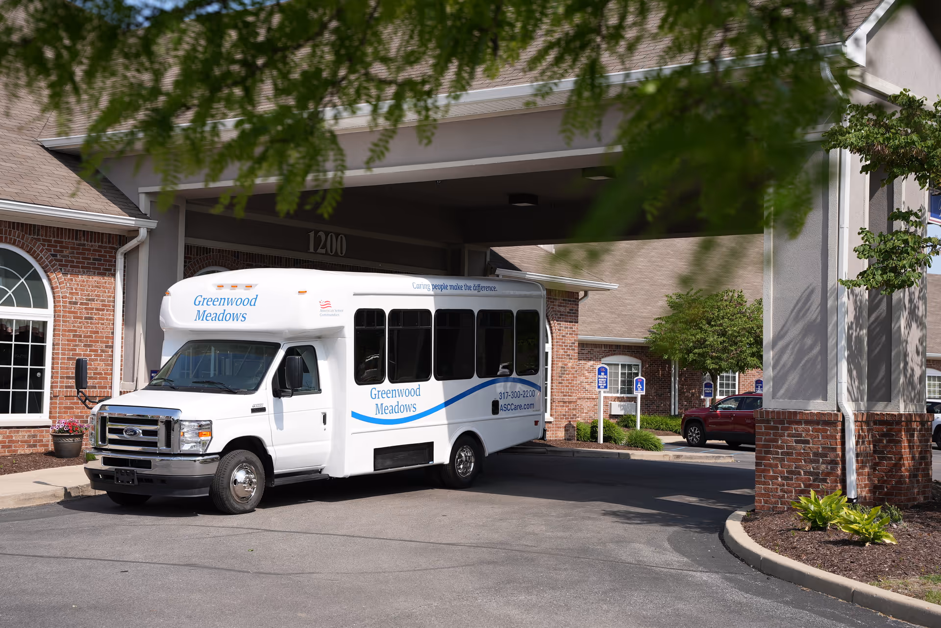 Greenwood Meadows shuttle parked at the front entrance of a brick senior living facility.