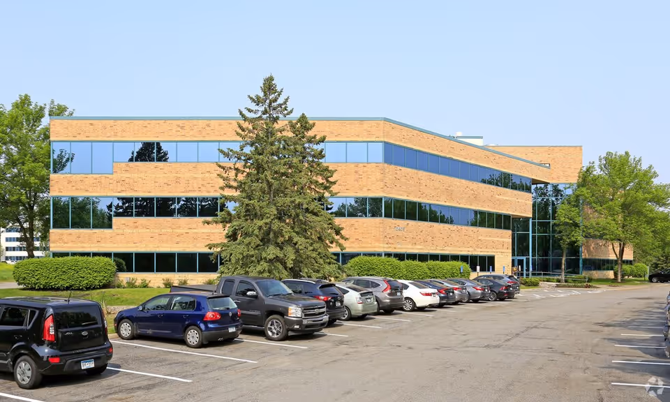 Brick exterior facility with large windows, a parking lot, and surrounding trees.