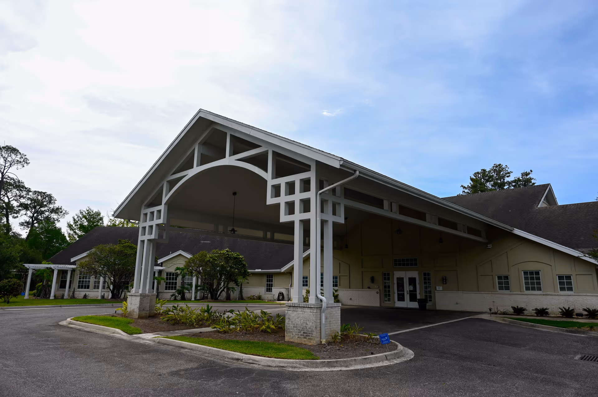 Exterior view of a senior living facility with a covered entrance and landscaped surroundings.
