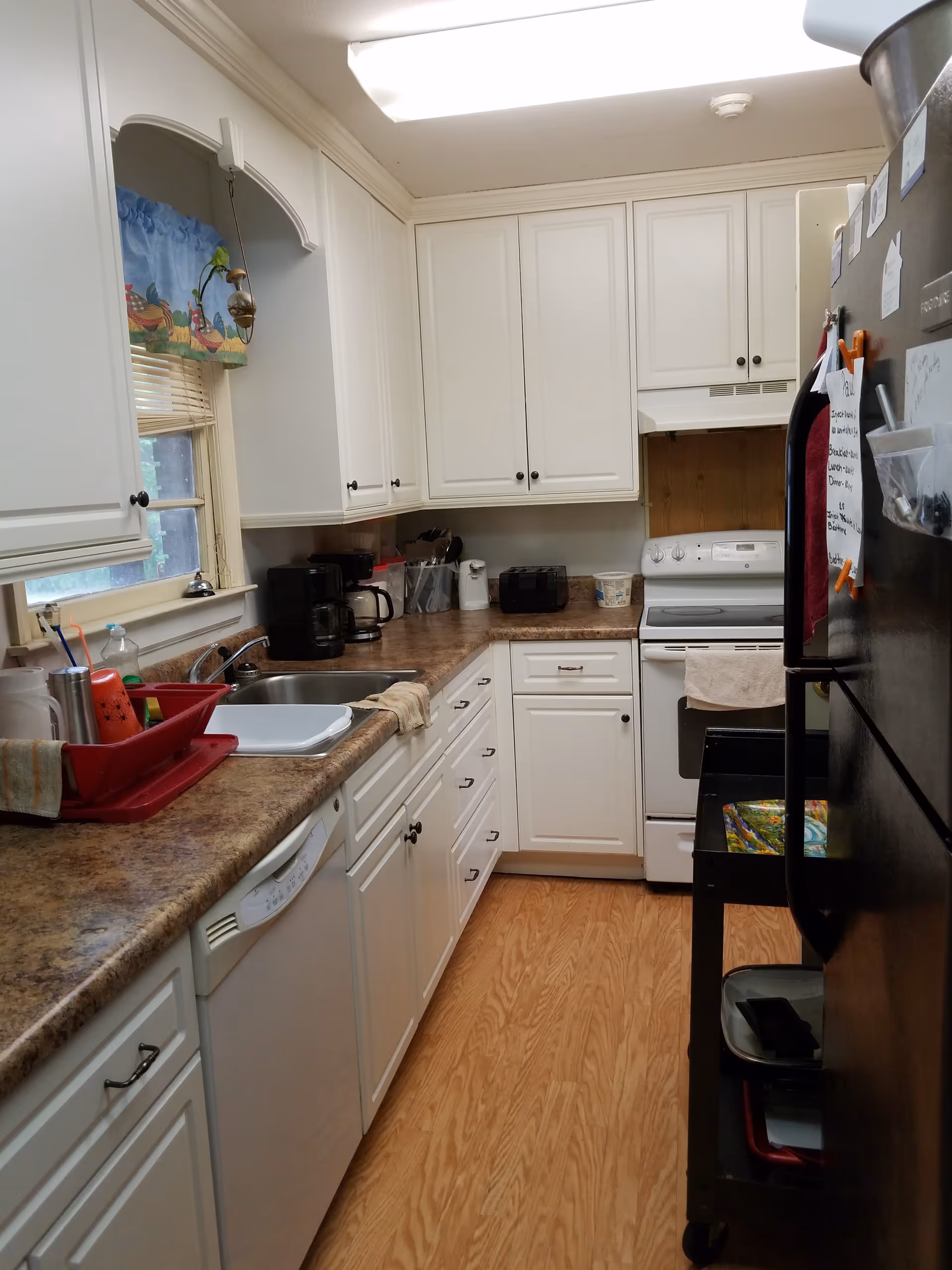 Bright white kitchen with cabinets, countertops, sink, and appliances in a senior living facility.