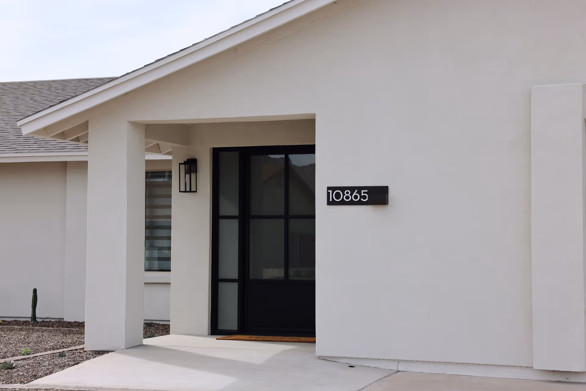 Modern beige building exterior with a black-framed glass entrance and address plaque.