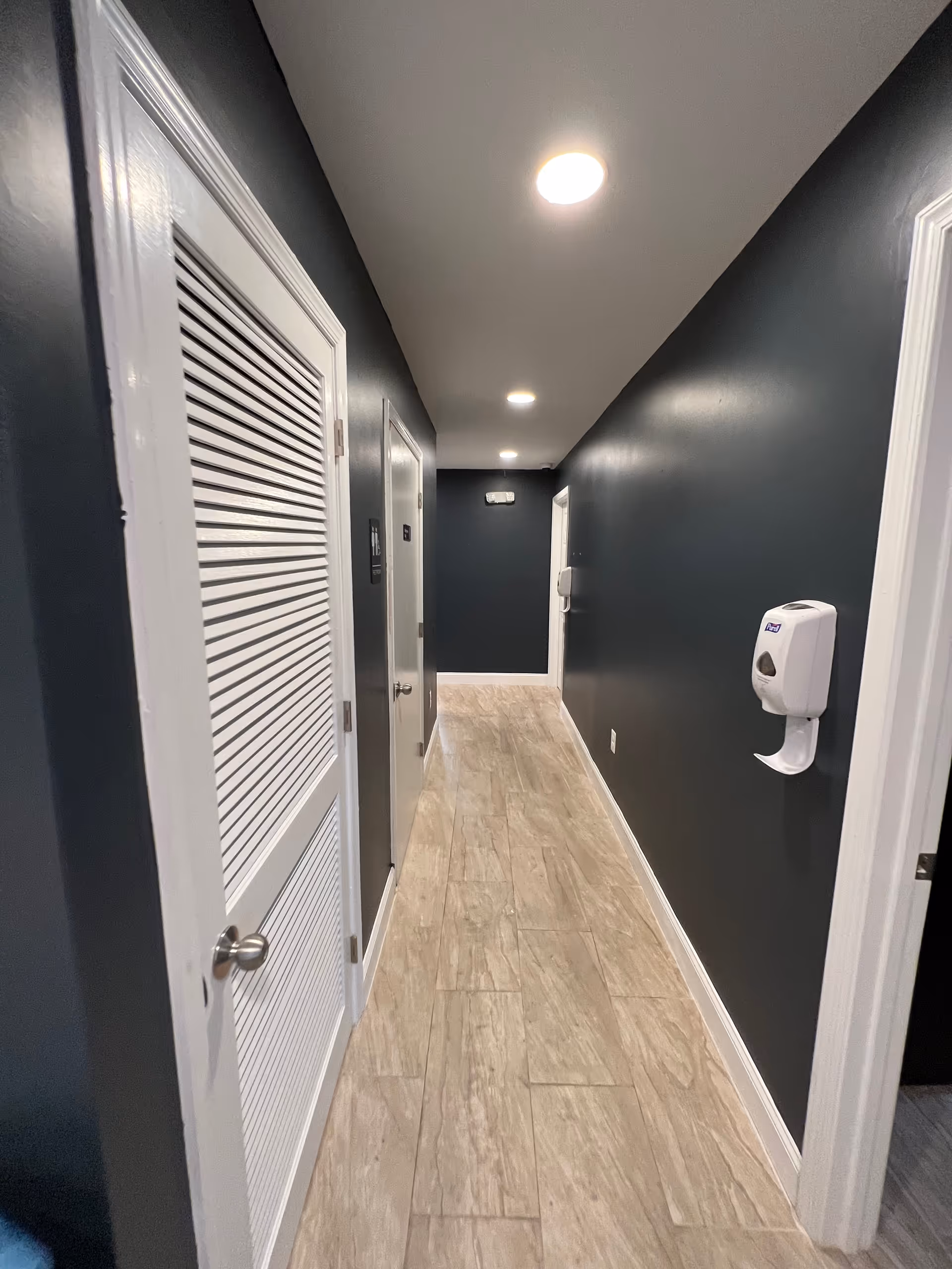 Dark hallway interior of a senior care facility with doors and a wall-mounted sanitizer dispenser.
