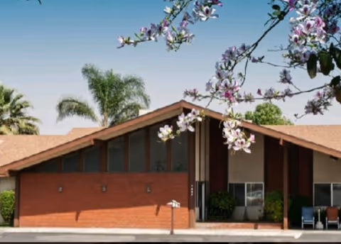 Front view of Rialto Assisted Living building with brick walls, peaked roof, and flowering branches.
