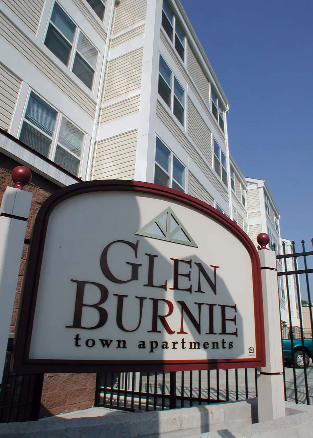 Exterior view of Glen Burnie Town Apartments sign with a multi-story apartment building and clear blue sky in the background.