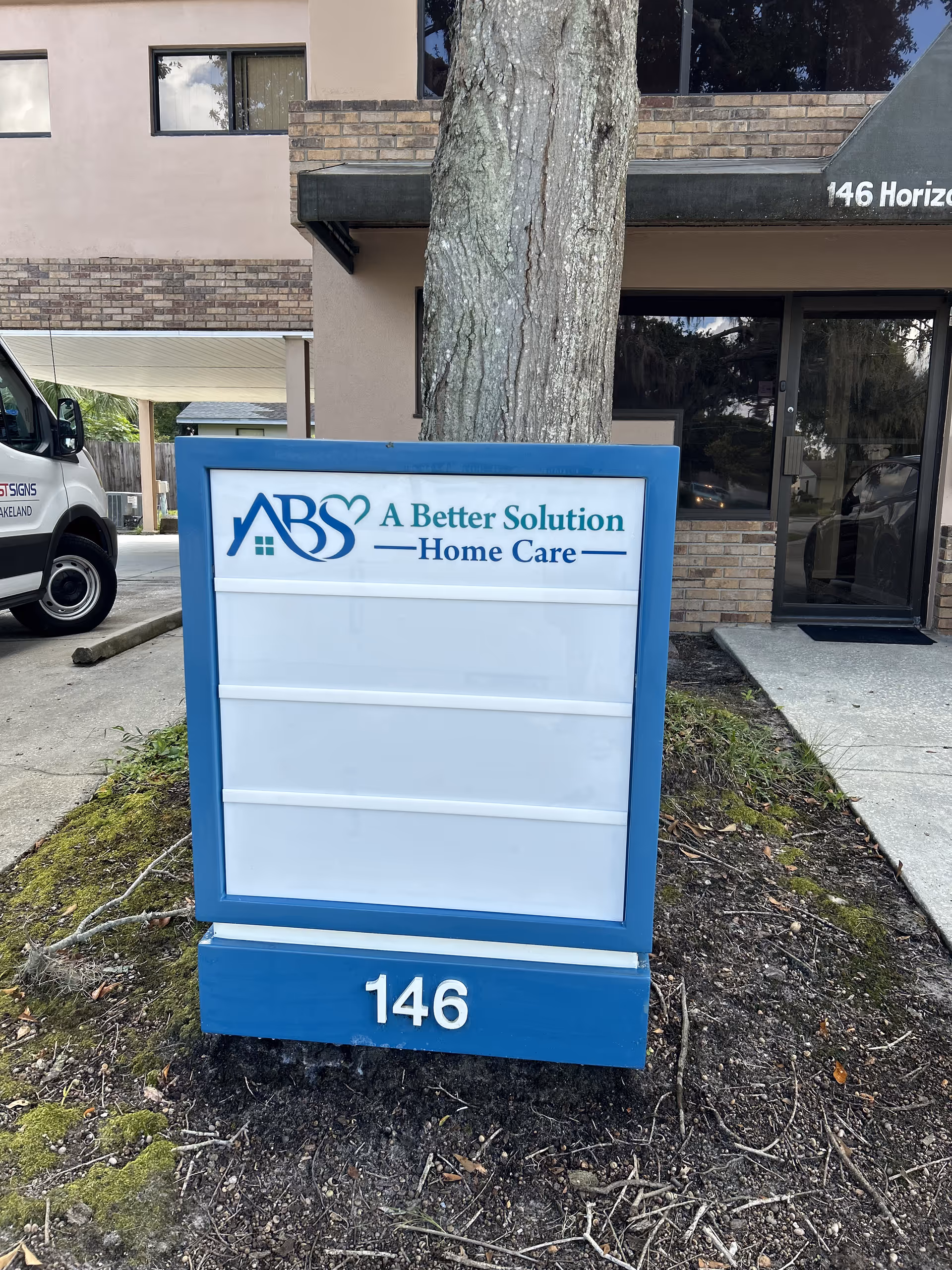 Blue-framed sign for A Better Solution Home Care sits in front of a brick building.
