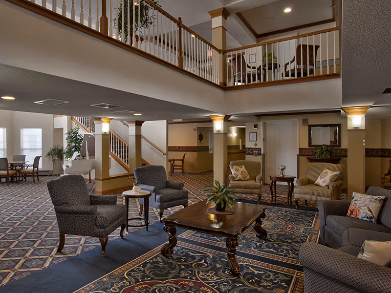 Spacious senior living lobby with sofas, coffee tables, and a second-floor balcony overlook.