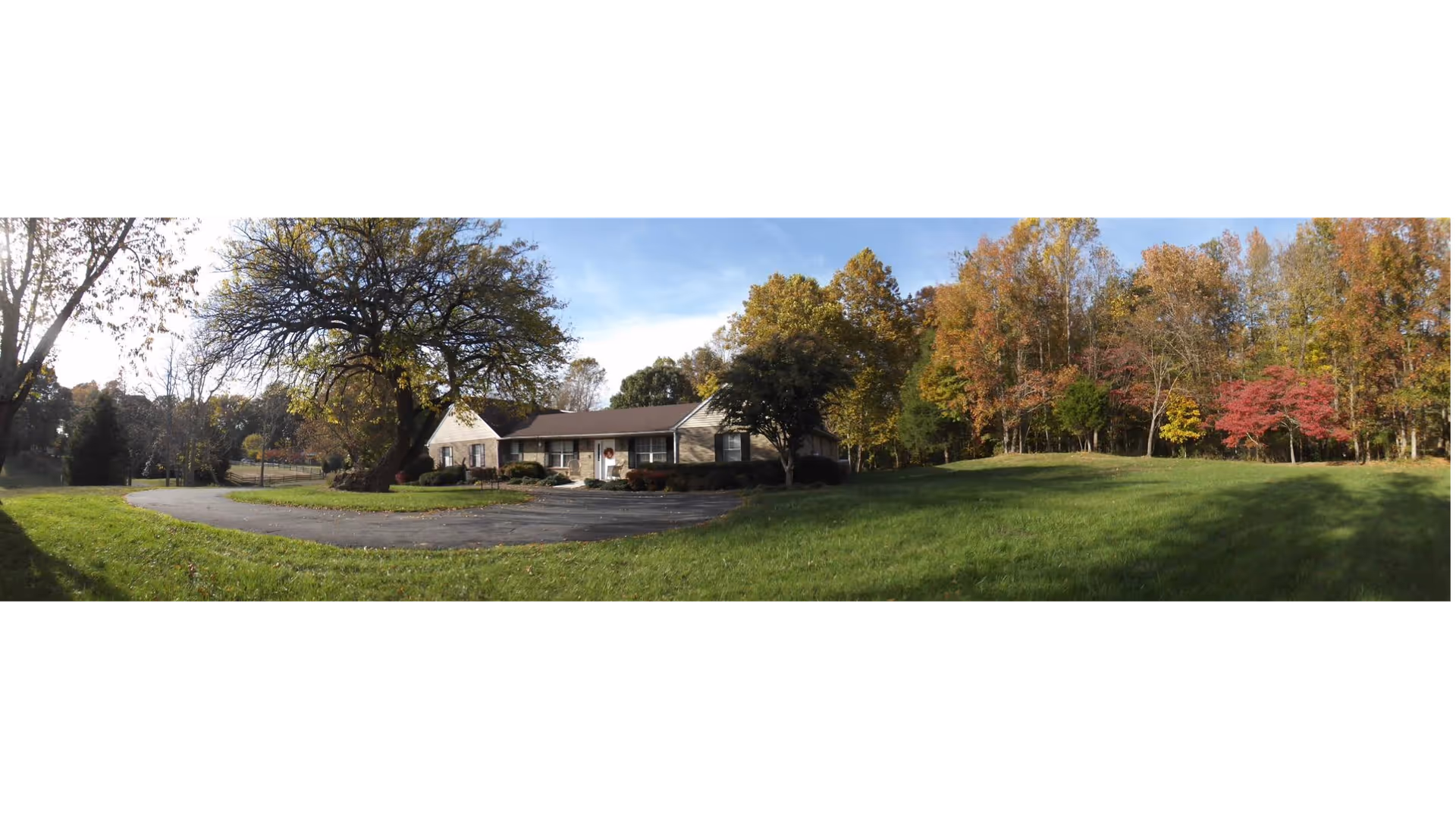 Panoramic exterior view of a single-story senior living facility surrounded by trees and lawn.