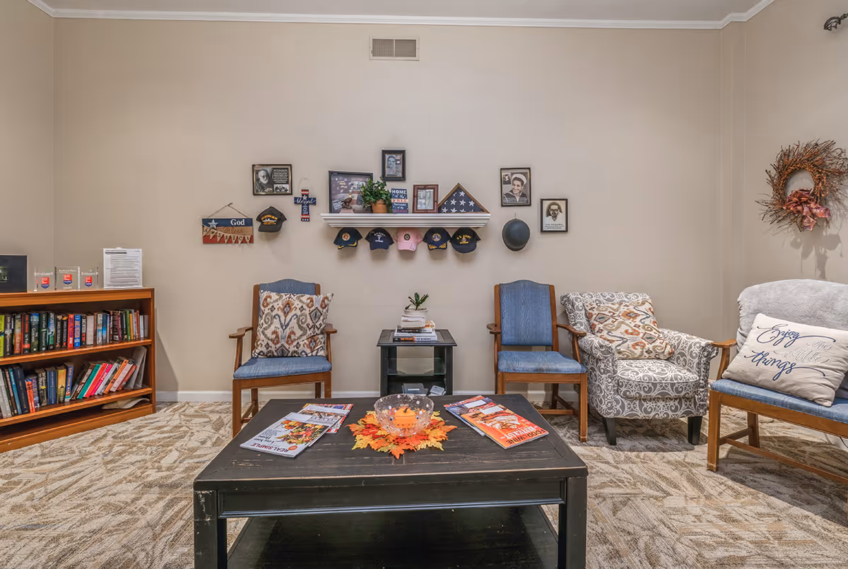 Cozy senior living lounge with blue chairs, coffee table, magazines, and wall décor.
