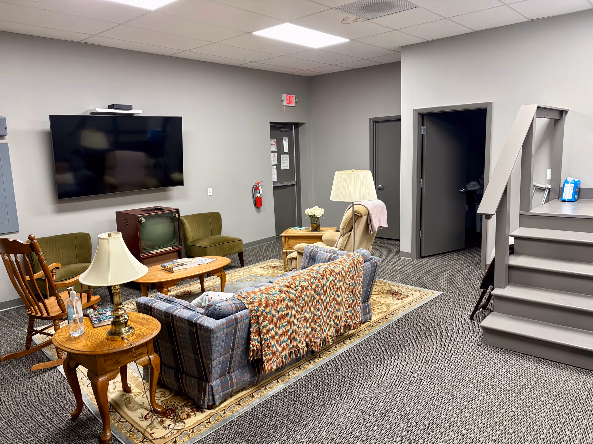 Cozy common living room with sofa, chairs, coffee tables, TV, and a staircase.