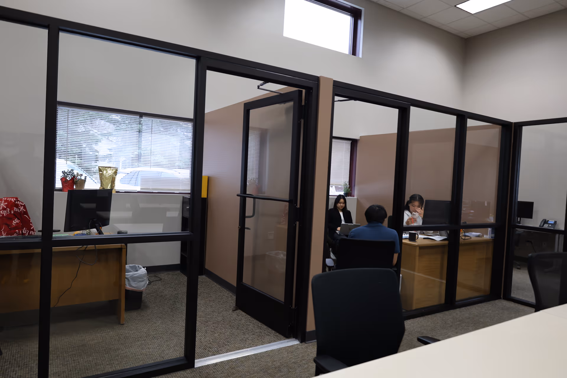 Office space with glass partitions and staff seated at desks inside cubicles.