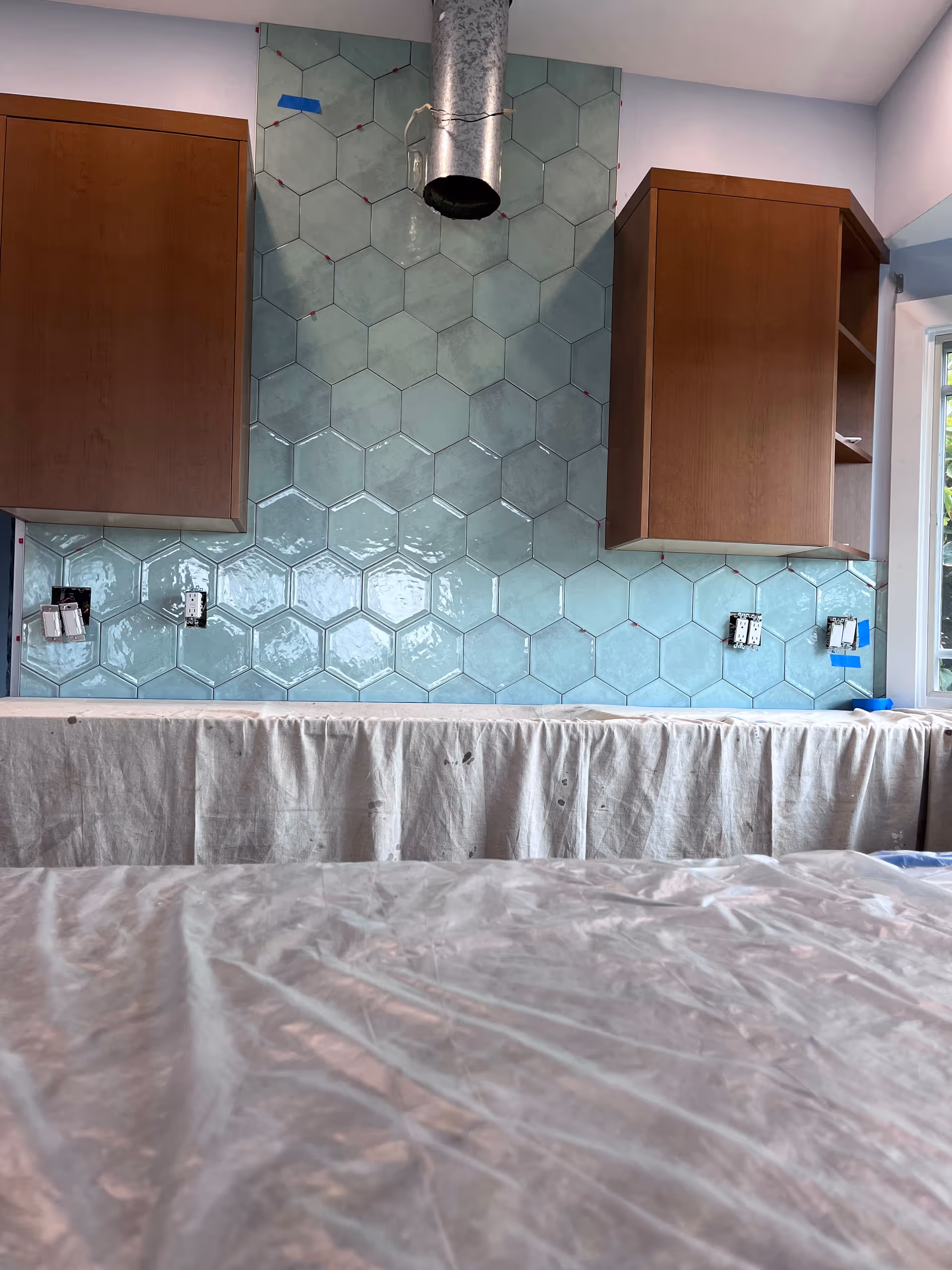 Under construction kitchen with blue hex tile backsplash and wooden cabinets.