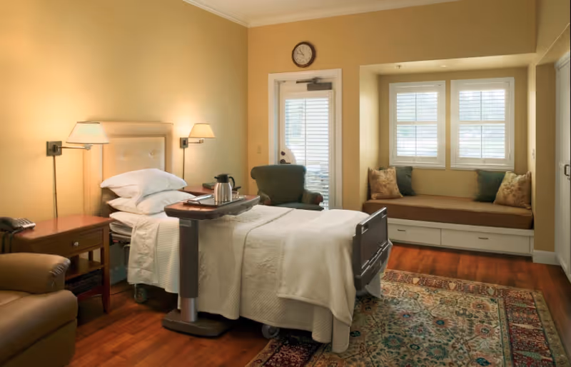 Hospital-style bedroom with bed, seating nook, and warm wood floors.