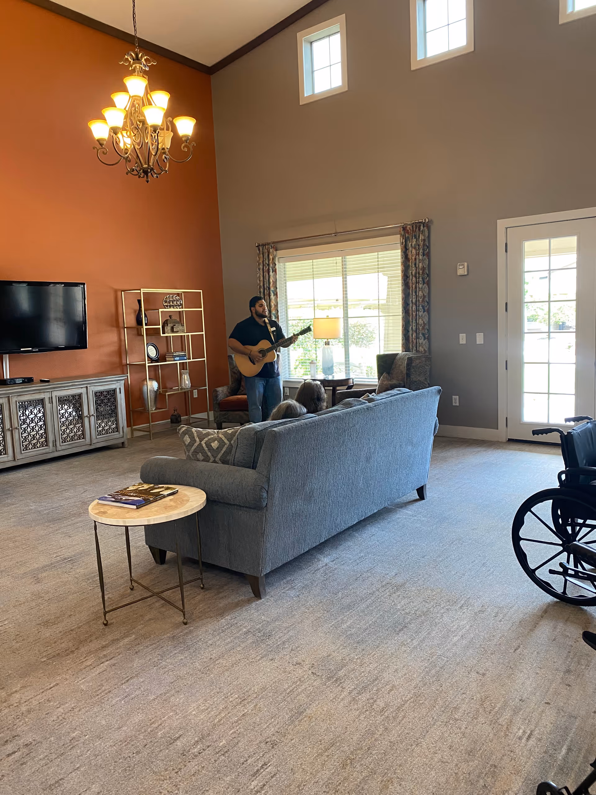 Guitarist performs in a spacious living room as residents sit on a couch.
