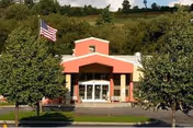 Front view of a red-orange building with glass doors, trees, and an American flag.