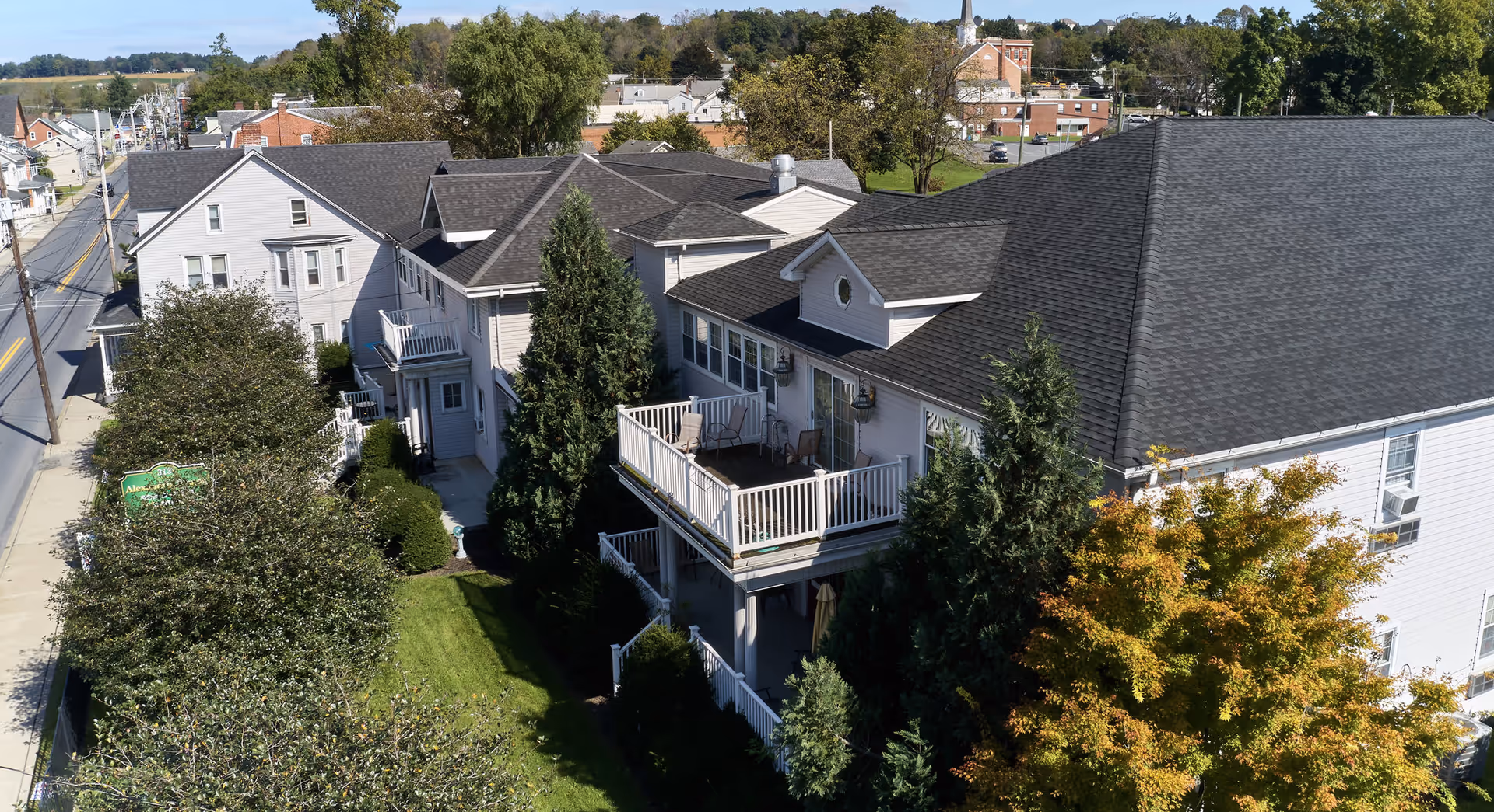 Aerial view of a multi-story senior living building with balconies, surrounding trees, and an adjacent street.