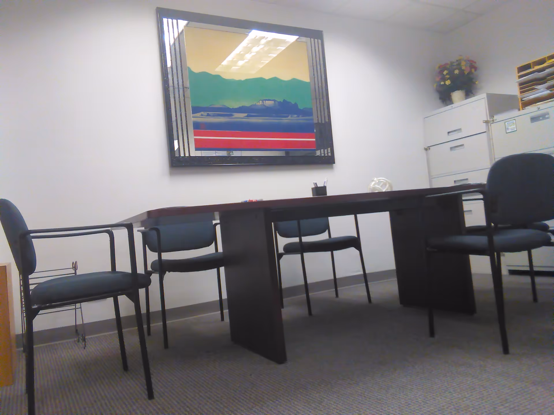A small conference room with a dark table, chairs, framed artwork, and filing cabinets.
