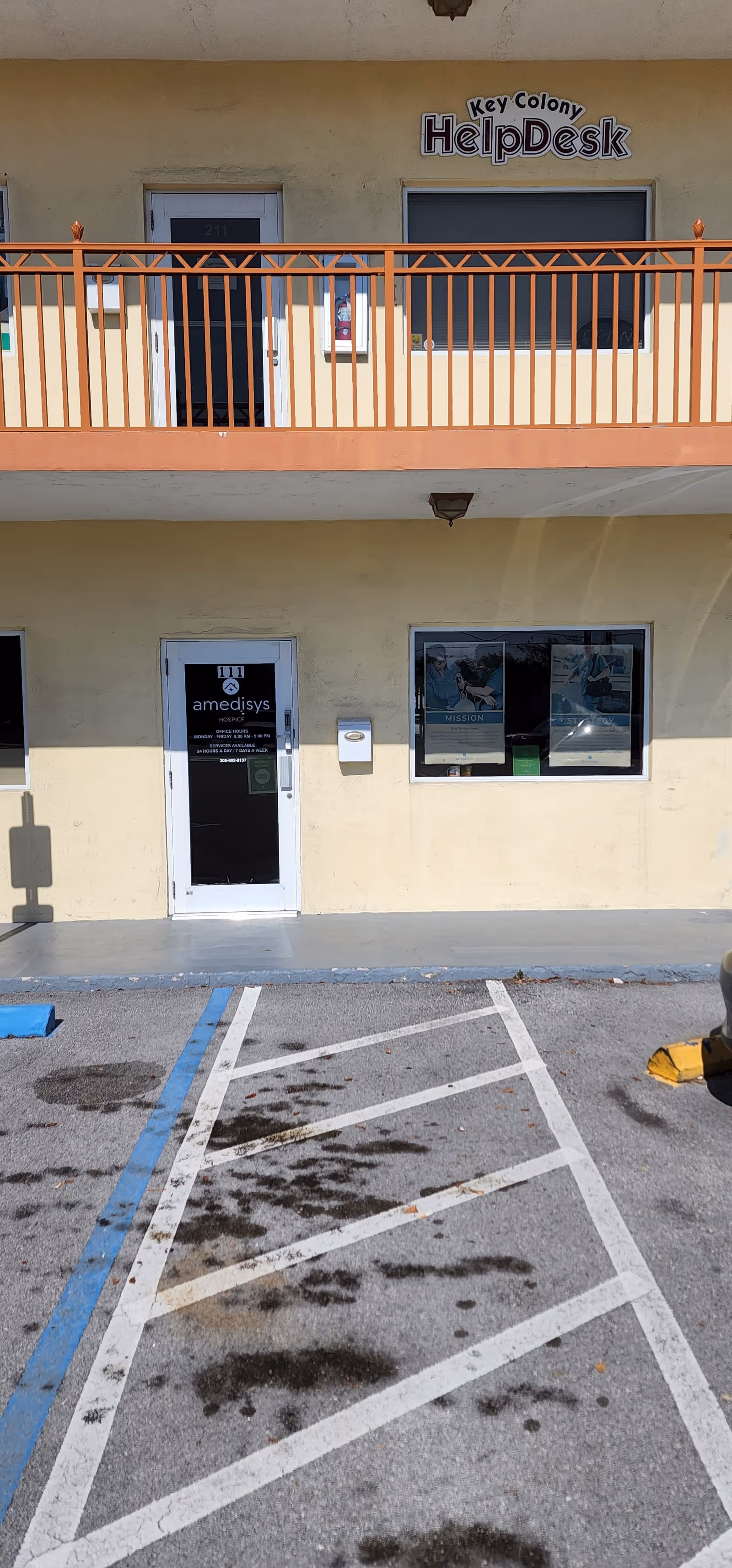 Two-story beige building with orange balcony railing, HelpDesk sign, and Amedisys Hospice door.