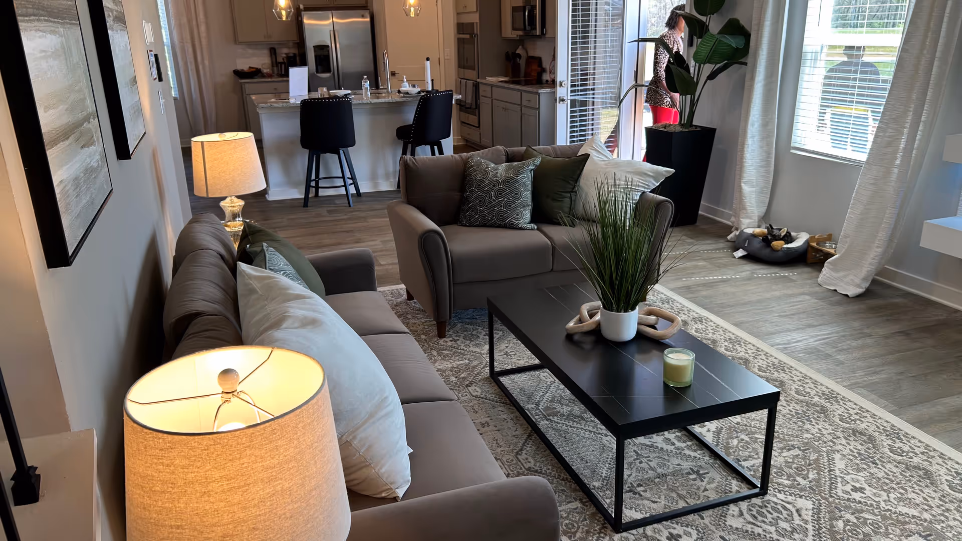 Open living room with sofa, coffee table, plants, and a kitchen island in back.
