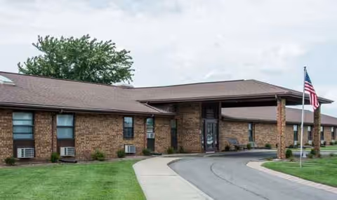 Single-story brick senior facility exterior with entrance, curved driveway, and flagpole.